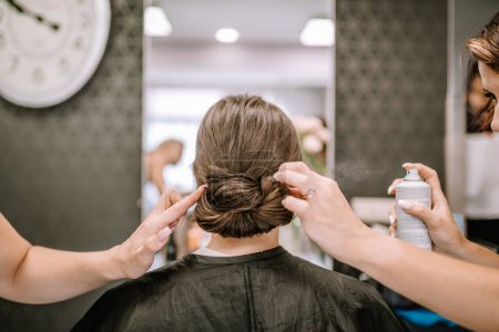Valmiera, Lettland - 19. August 2023 - Stylisten perfektionieren die komplizierte Dutt-Frisur einer Frau in einem Salon.
