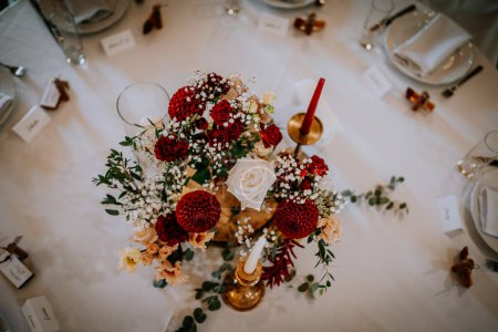 Photo for Valmiera, Latvia - August 19, 2023 - Top-down view of a wedding table centerpiece featuring red and white roses, baby's breath, and other flowers, with a golden candle holder. - Royalty Free Image