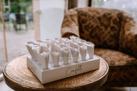 Valmiera, Latvia - August 19, 2023 - A box of white paper cones filled with flower petals placed on an ornate table, with an elegant sofa in the background.
