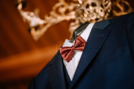 Valmiera, Latvia - August 19, 2023 - Close-up of a man's suit jacket with a red bow tie and white shirt, set against an ornate golden background.