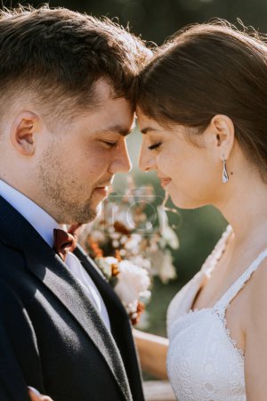 Foto de Valmiera, Letonia - 19 de agosto de 2023 - Un retrato de cerca de una novia y un novio tocando la frente, profundamente enamorados, con la luz del sol iluminando sus rostros. - Imagen libre de derechos