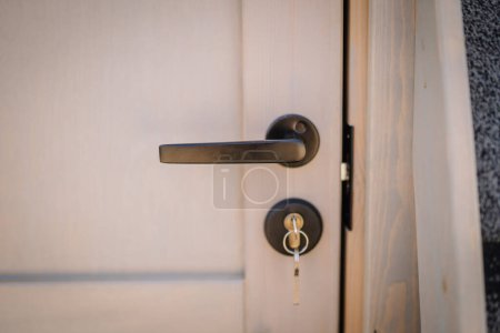 Téléchargez les photos : Gros plan d'une poignée de porte moderne et serrure sur une porte en bois avec une clé insérée, sur un fond flou. - en image libre de droit