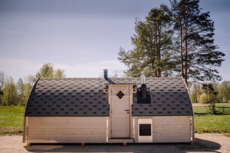 Téléchargez les photos : Une petite cabane en bois avec un toit en bardeaux, avec deux cheminées et une porte d'entrée, située dans un cadre extérieur herbeux. - en image libre de droit
