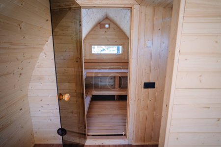 Vue intérieure d'une petite pièce en bois avec un escalier en bois intégré menant à un loft, avec une fenêtre cintrée à l'extrémité.