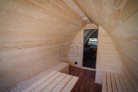 Vista interior de una cabaña de madera con paredes arqueadas y techo, con bancos de madera incorporados y una puerta que conduce a otra habitación.