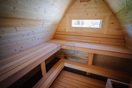 Interior view of a small cabin loft with wooden benches and a window, all surfaces covered in natural pine wood.