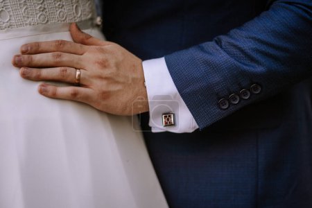 Photo for Valmiera, Latvia - August 19, 2023 - Close-up of a groom's hand on a bride's waist, showing his wedding ring, cufflink, and details of their wedding attire. - Royalty Free Image