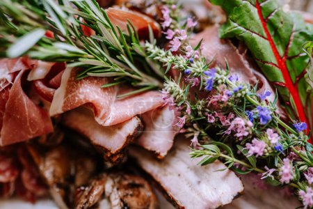 Valmiera, Latvia - August 19, 2023 - Extreme close-up of a gourmet meat platter adorned with fresh herbs and edible flowers, displaying a mix of textures and colors.