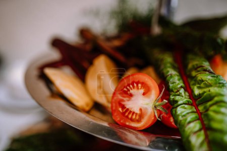 Valmiera, Latvia - August 19, 2023 - Close-up of a fresh tomato slice alongside cooked chard and pear slices on a serving platter.