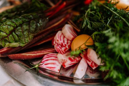 Valmiera, Latvia - August 19, 2023 - Close-up of vibrant, fresh vegetables including chard, candy-striped beet slices, and herbs on a metal platter.