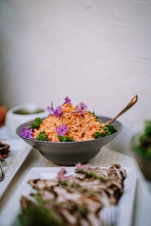 Valmiera, Lettonie - 19 août 2023 - Un bol de salade de carottes garni de fleurs comestibles violettes et d'herbes vertes, présenté élégamment lors d'un dîner.