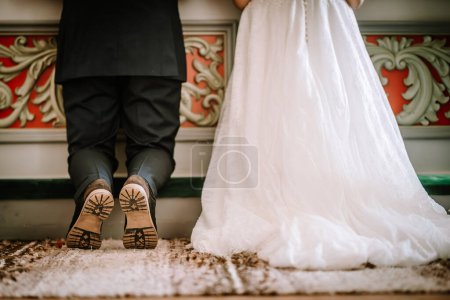 Photo for Valmiera, Latvia - August 25, 2023 - Close-up of a bride and groom's feet showing the groom's unique footwear and the bride's flowing wedding dress against a decorative backdrop. - Royalty Free Image
