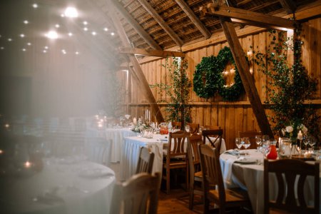 Valmiera, Letonia - 25 de agosto de 2023 - Lugar de boda rústico con vigas de madera, mesas de comedor con velas y vegetación en las paredes.