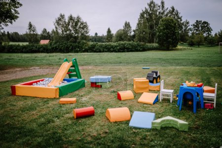 Valmiera, Latvia - August 25, 2023 - Outdoor children's play area with colorful equipment, including a slide, mats, and toys on grass.