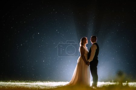 Valmiera, Lettland - 25. August 2023 - Ein Paar steht Hand in Hand unter einem Sternenhimmel, umgeben von schwebenden Lichtflecken.