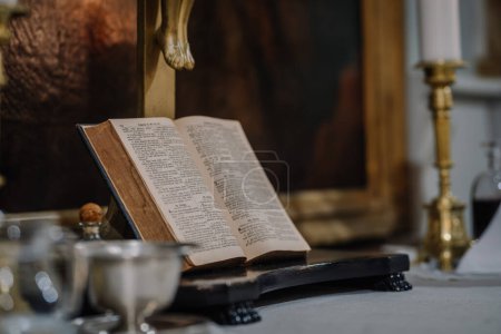 Foto de Valmiera, Letonia - 12 de mayo de 2024 - una Biblia abierta sobre un atril en un entorno eclesiástico, rodeada de velas y un cáliz. - Imagen libre de derechos