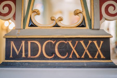 Valmiera, Letonia - 12 de mayo de 2024 - Números romanos MDCCXX sobre un pedestal decorativo de madera con detalles ornamentados.