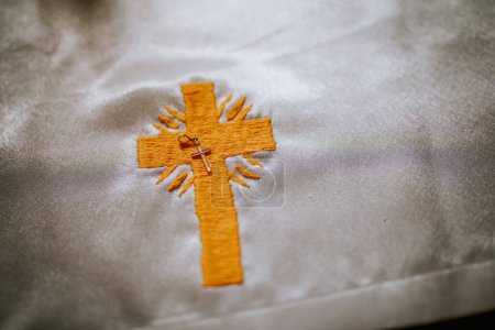 Valmiera, Lettland - 12. Mai 2024 - Nahaufnahme eines bestickten Kreuzes mit einem kleinen Metallkreuz-Anhänger auf einem Stoff.