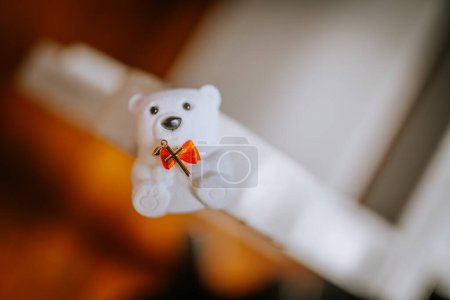 Valmiera, Latvia - May 12, 2024 - White teddy bear holding a red bow and a gold cross, on a light background.