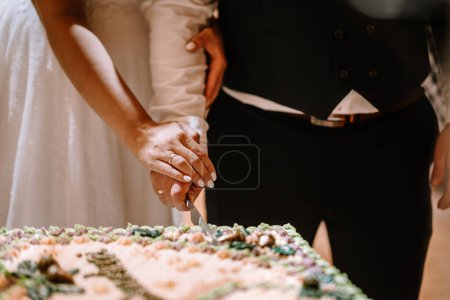 Valmiera, Latvia - August 25, 2023 - Bride and groom cutting wedding cake together, close-up of hands with a knife.