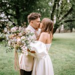 Riga, Latvia, - August 26, 2024 - Bride and groom kissing in park, bride holding large floral bouquet.