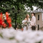 Riga, Latvia, - August 26, 2024 - Bride and groom standing in a park, with white flowers in the foreground.