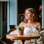 Riga, Latvia, - August 26, 2024 - Bride seated in a cafe, looking thoughtfully out the window, with a bouquet on the table.