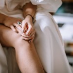 Riga, Latvia, - August 26, 2024 - Hands resting on a knee, wearing a white dress, showcasing rings and painted nails in a soft, elegant, and relaxed setting.