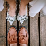 Riga, Latvia, - August 26, 2024 - Close-up of a bride and groom's shoes on a wooden deck, showcasing a contrast in styles.