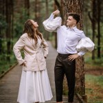 Riga, Latvia, - August 26, 2024 - Bride and groom playfully posing, showing off muscles on a forest walkway.