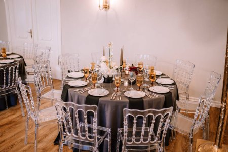 Riga, Latvia, - August 26, 2024 - Sophisticated wedding reception setting featuring black tablecloths, gold-rimmed glassware, floral centerpieces, and clear chairs in an elegant room.