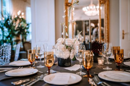 Riga, Latvia, - August 26, 2024 - Close-up of a wedding reception table with black tablecloth, gold glassware, white floral centerpieces, and elegant room decor in the background.