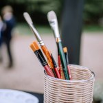 Riga, Latvia, - August 26, 2024 - Close-up of assorted paintbrushes in a wicker basket, with a blurred background showing people outdoors.