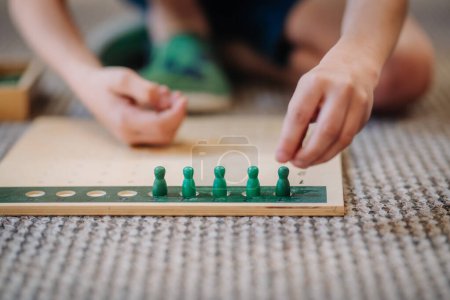 Valmiera, Letonia - 22 de mayo de 2024 - Manos de niño jugando con piezas de juegos educativos verdes en una tabla de madera, colocadas en un piso alfombrado.