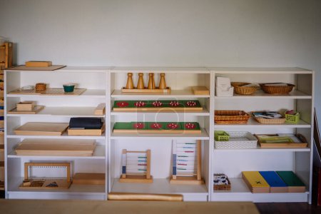 Regale in einem Montessori-Klassenzimmer, gefüllt mit verschiedenen pädagogischen Werkzeugen und Materialien, fein säuberlich geordnet für Lernaktivitäten. Der Raum ist aufgeräumt und hell.