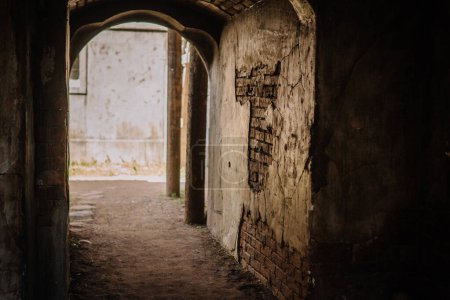 Dobele, Latvia - June 7, 2024 - Dark, narrow passageway with an arched ceiling, leading to a brighter, open area. The walls are weathered and textured, creating a mysterious atmosphere.