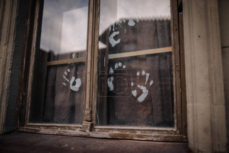 Dobele, Latvia - June 7, 2024 - Close-up of a weathered window with white handprints on the glass, creating a mysterious and eerie atmosphere.
