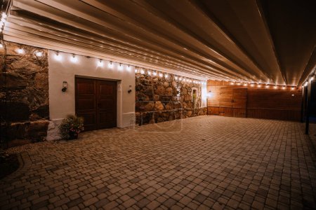 Blome, Latvia - September 11, 2023 - Outdoor covered area with stone walls, wooden doors, and string lights at night, creating a warm and inviting atmosphere.