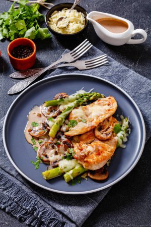 Chicken Madeira, juicy chicken breasts and mushrooms in a madeira cream sauce under melty mozzarella cheese and asparagus on plate, vertical view
