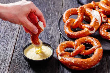 mujer sumerge un pedazo de pretzel suave en salsa de queso, vista horizontal desde arriba, primer plano