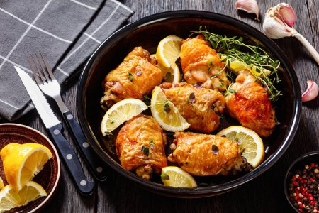 cuisses de poulet dorées et croustillantes cuites au four avec du citron, du thym et des épices dans un plat de cuisson sur une table en bois sombre