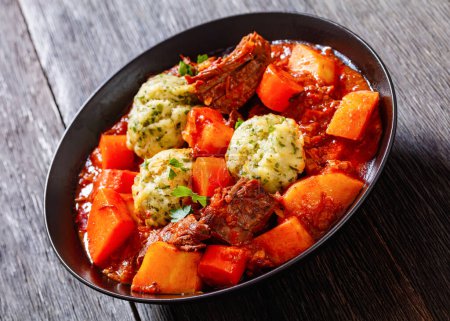 Estofado de ternera con albóndigas y verduras en tomate rico y salsa a base de caldo en tazón negro, primer plano