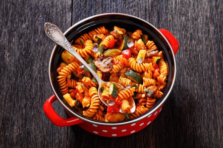 One Pot Veggie Pasta of rotini, zucchini, capsicum, mushrooms smothered in a garlic herb tomato sauce in red pot on dark wood table