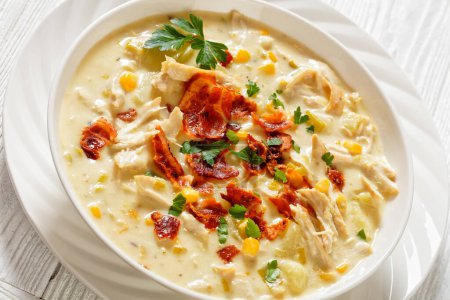 Chicken Corn Chowder, rich and creamy soup with leftover chicken breast, potatoes, sweet corn, topped with fried crispy bacon and fresh parsley in white bowl, close-up