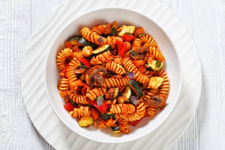 One Pot Vegetable Pasta of rotini, zucchini, capsicum, mushrooms smothered in a garlo c herb tomato sauce in white bowl on white wooden tablei, flat lay