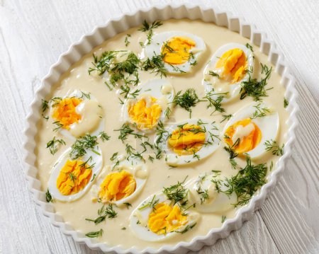 Senfeier,  hard boiled eggs in rich creamy mustard sauce in white baking dish on white wood  table, German cuisine, close-up