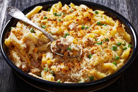 Tuna Mornay, Creamy Tuna Casserole Penne Pasta Bake in baking dish on dark wooden table with spoon, close-up