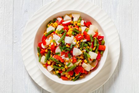 Charred Corn, Radish, Jicama, Red pepper and Green Bean Vegan Salad with Lime Olive oil Dressing in white bowl on white wood table, horizontal view from above, flat lay, close-up