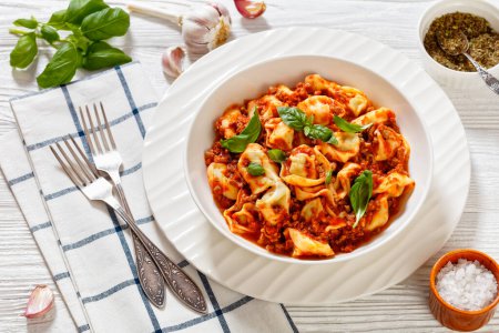 tortellini in ground beef tomato sauce in white bowl on white wood table with forks