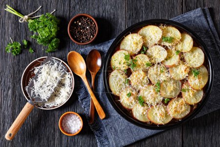 baked in oven Ground Beef stew with mushrooms and carrots topped with potatoes in baking dish on dark wood table with spoons, horizontal view from above, flat lay